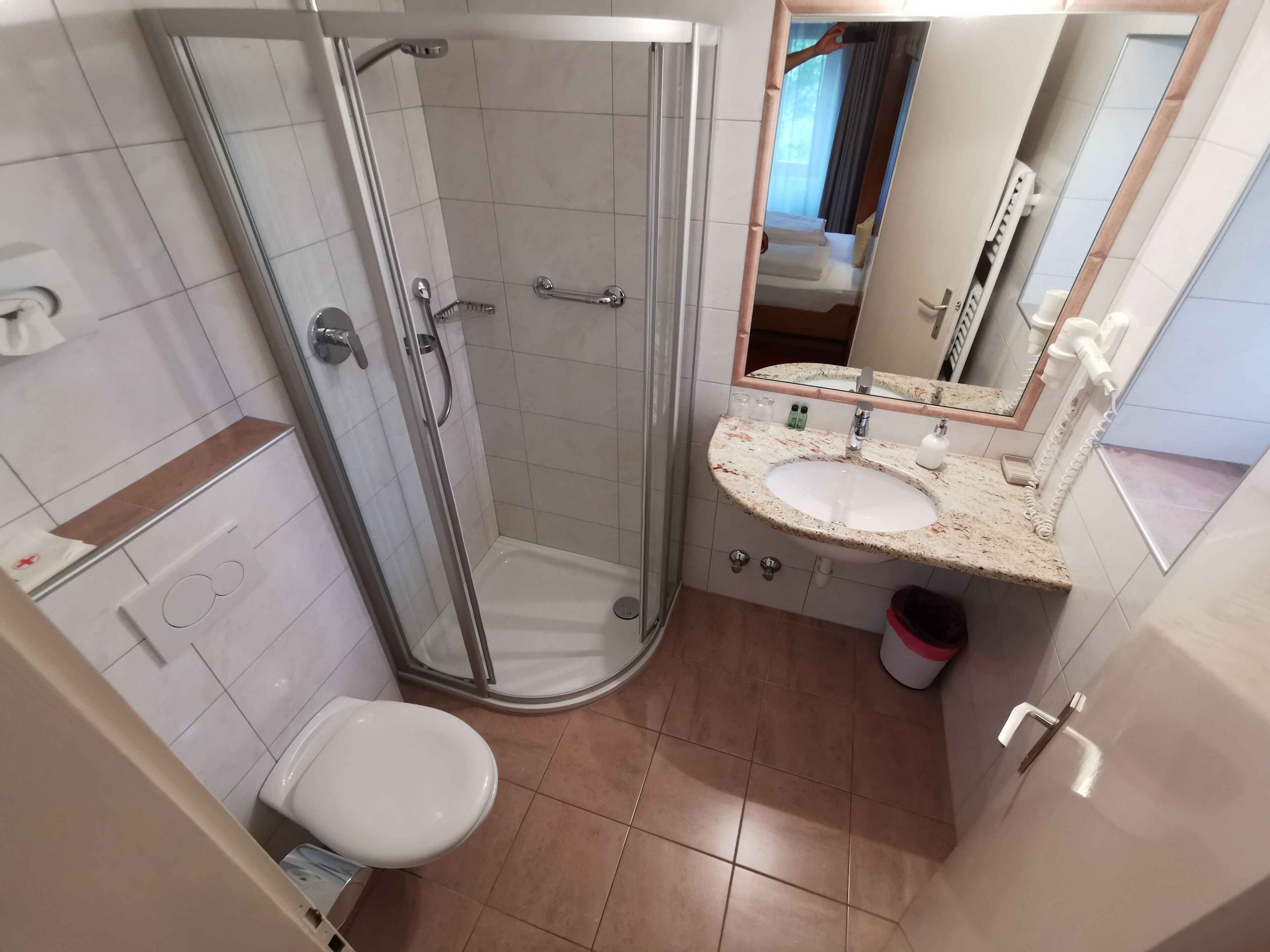 Un bagno moderno con doccia vetro, un water bianco, un lavandino con piano in marmo e uno specchio con cornice in legno.