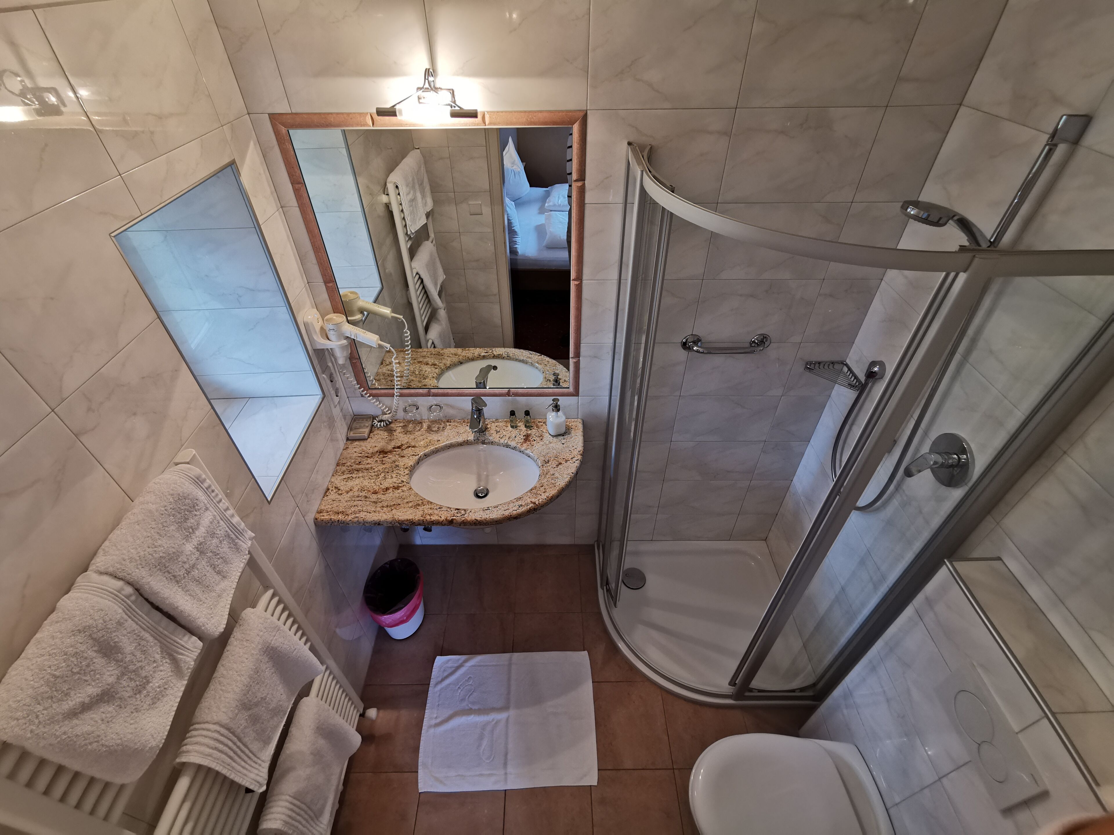 Une salle de bain avec un lavabo surmonté d’un plan de travail en granit, un miroir, une cabine de douche en verre et des toilettes.