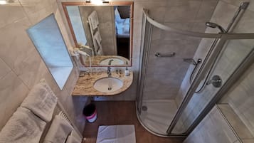 A bathroom with a granite countertop sink, a mirror, a glass shower enclosure, and a toilet.