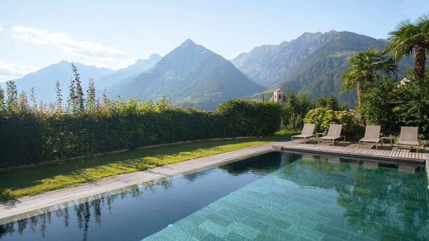 A clear infinity pool with a wooden deck, lounge chairs, and a view of mountains. -  Active B&B Prairerhof (Schenna)