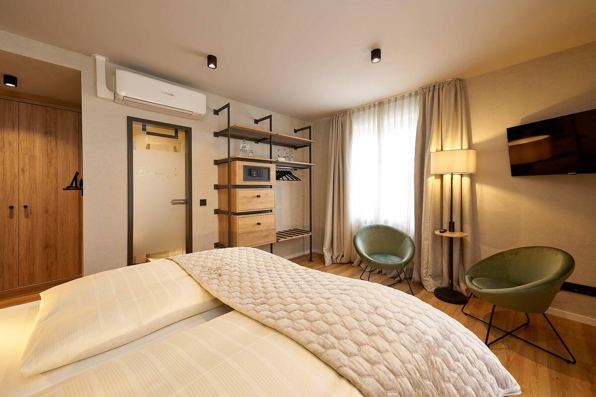 A modern hotel room with a bed, built-in wardrobe, shelves, a chair, and a TV.