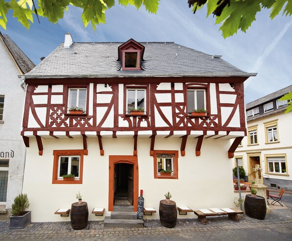 Un bâtiment traditionnel à colombages, doté d’une entrée centrale, de plantes en pot sur les rebords de fenêtres et situé sur une rue pavée.