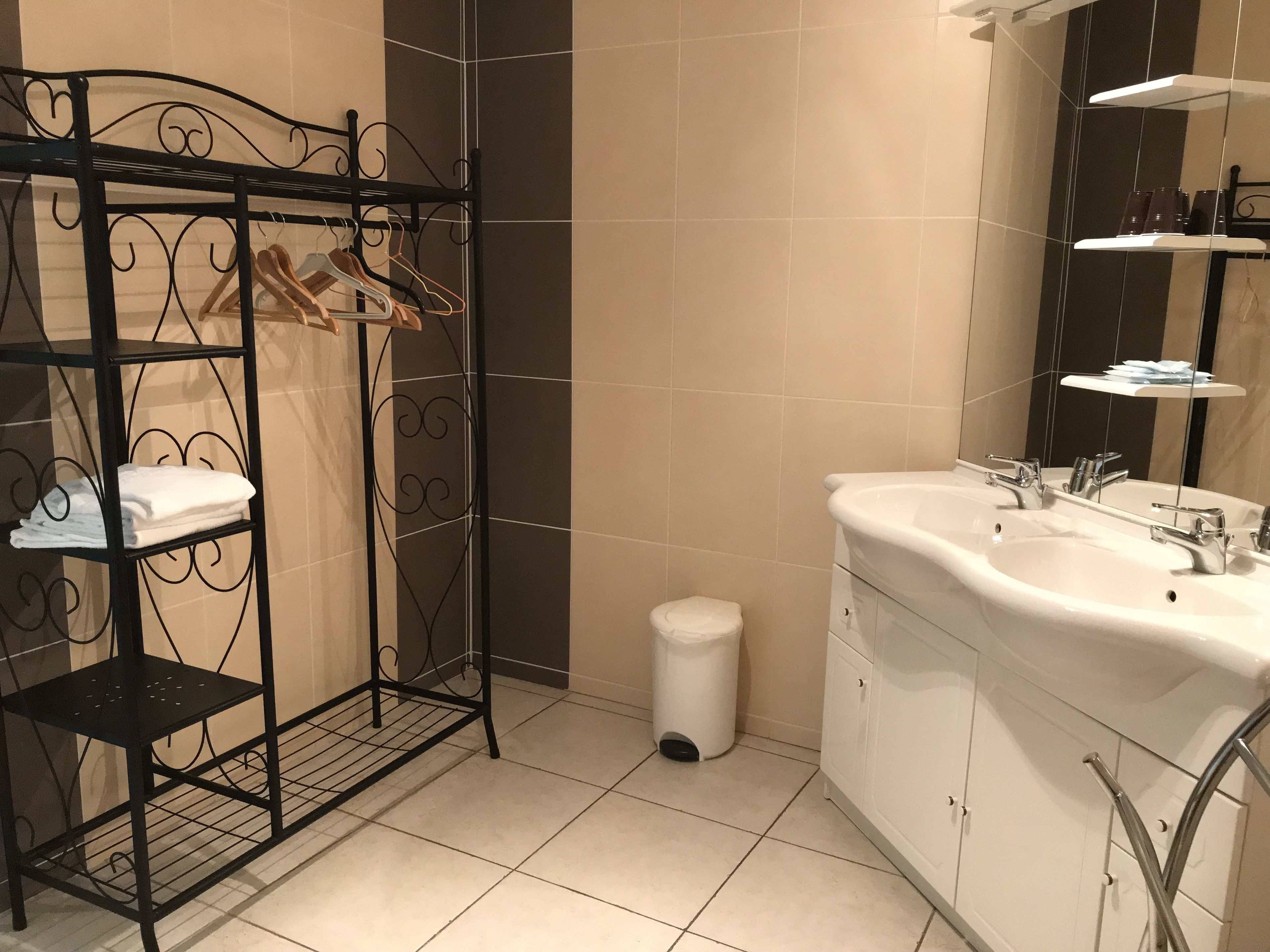 Een badkamer met een metalen rek met handdoeken en ophanghaakjes, een witte wastafel met spiegel, en een toilet.