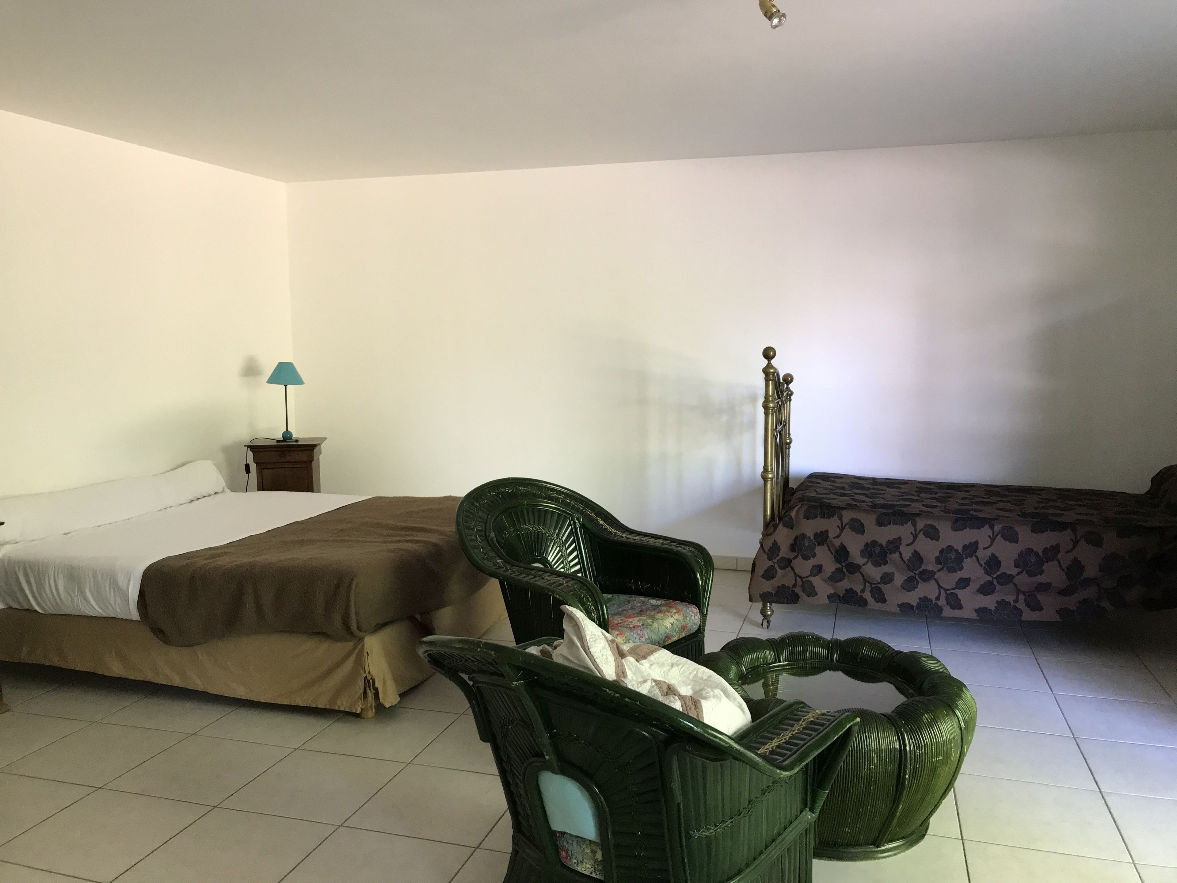 A room with a bed, a chair, a nightstand with a lamp, and a window.