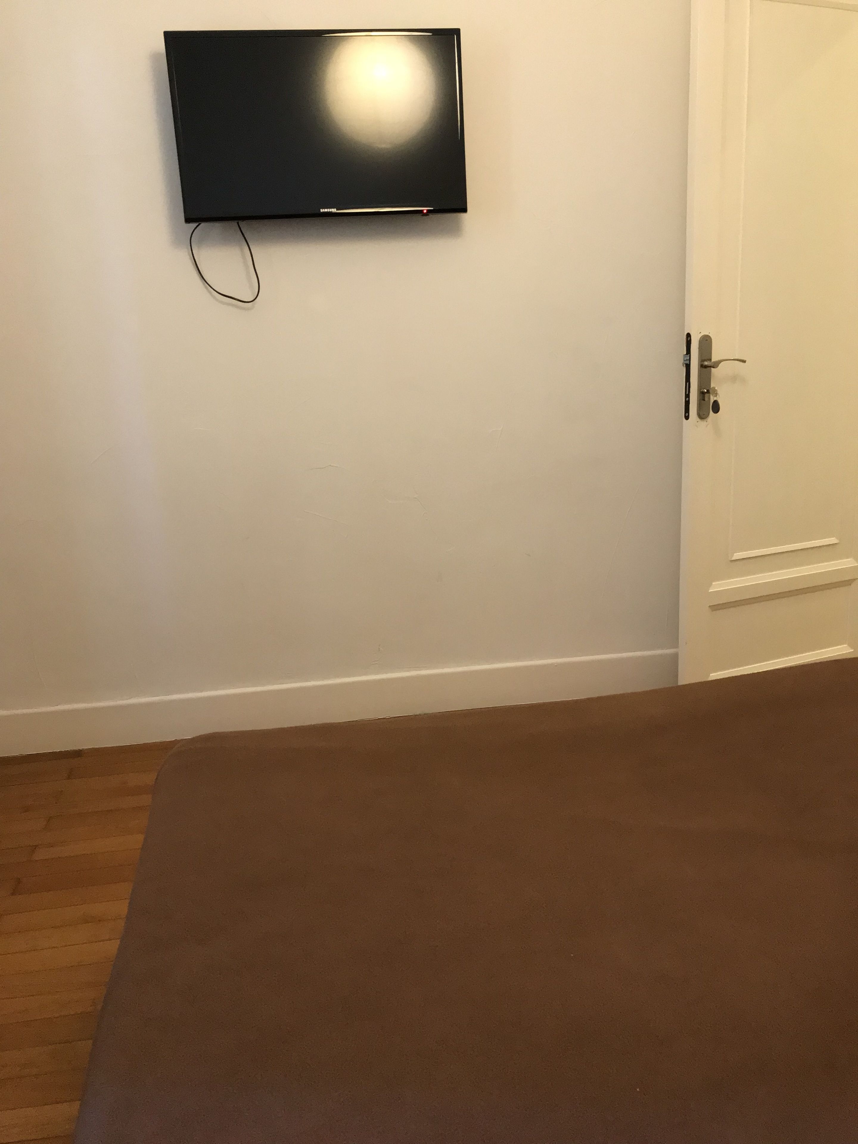 A room with a flat-screen TV mounted on the wall, a white door, and a brown carpet.