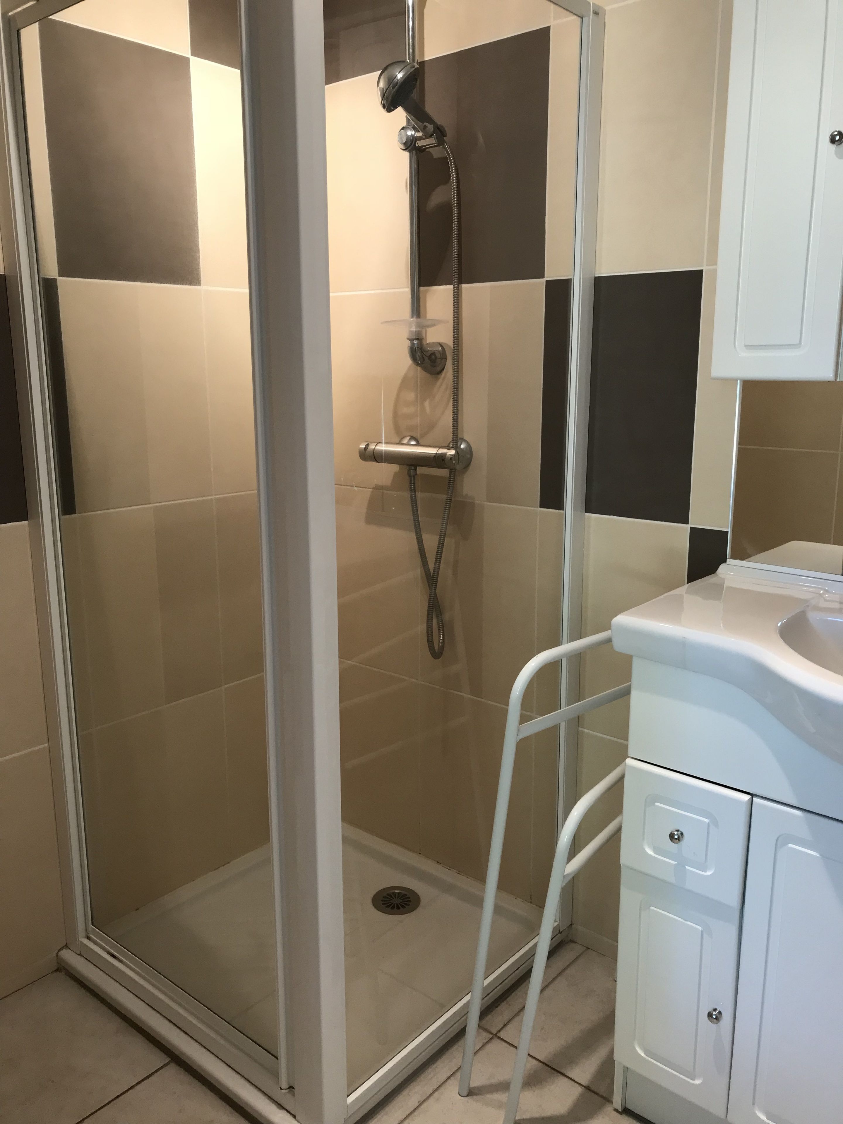 Un box de ducha con puerta de vidrio, un cabezal de ducha de mano y un grifo instalado en la pared.