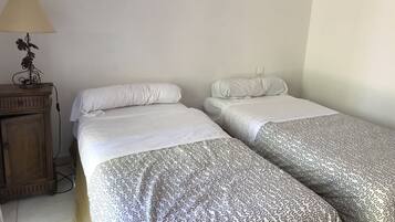 A room with two single beds, a wooden nightstand with a lamp, and a power outlet on the wall.