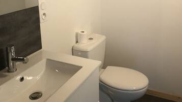 Une salle de bain avec un lavabo blanc, des toilettes et un miroir.