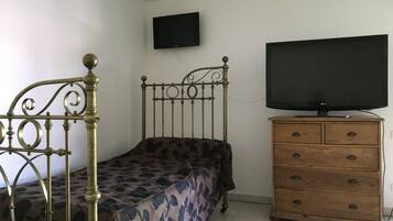 Quarto com estrutura de cama em metal, cómoda de madeira e televisão na parede.
