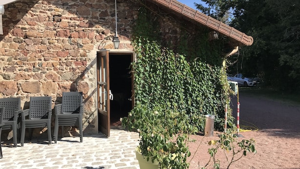 Un bâtiment en pierre avec une porte en bois, des sièges à l’extérieur et une plante en pot.