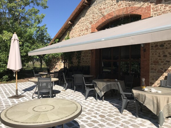 An outdoor patio with tables and chairs, a large umbrella, and a stone building in the background.