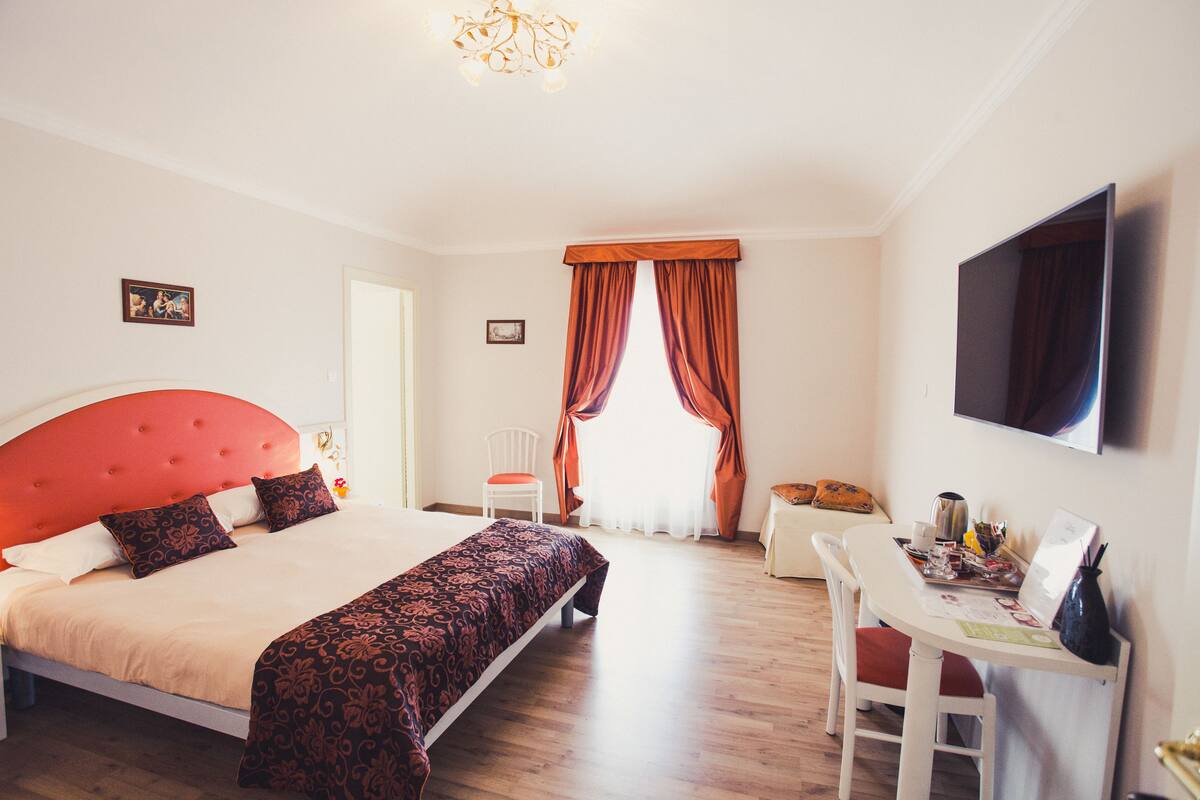 A hotel room with a large bed, a desk with a chair, a television, and a window with curtains.