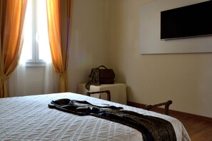 A hotel room with a bed, a chair, a small table, a television on the wall, and a window with curtains. - Casa Faccioli B&B Wellness (Bologna)