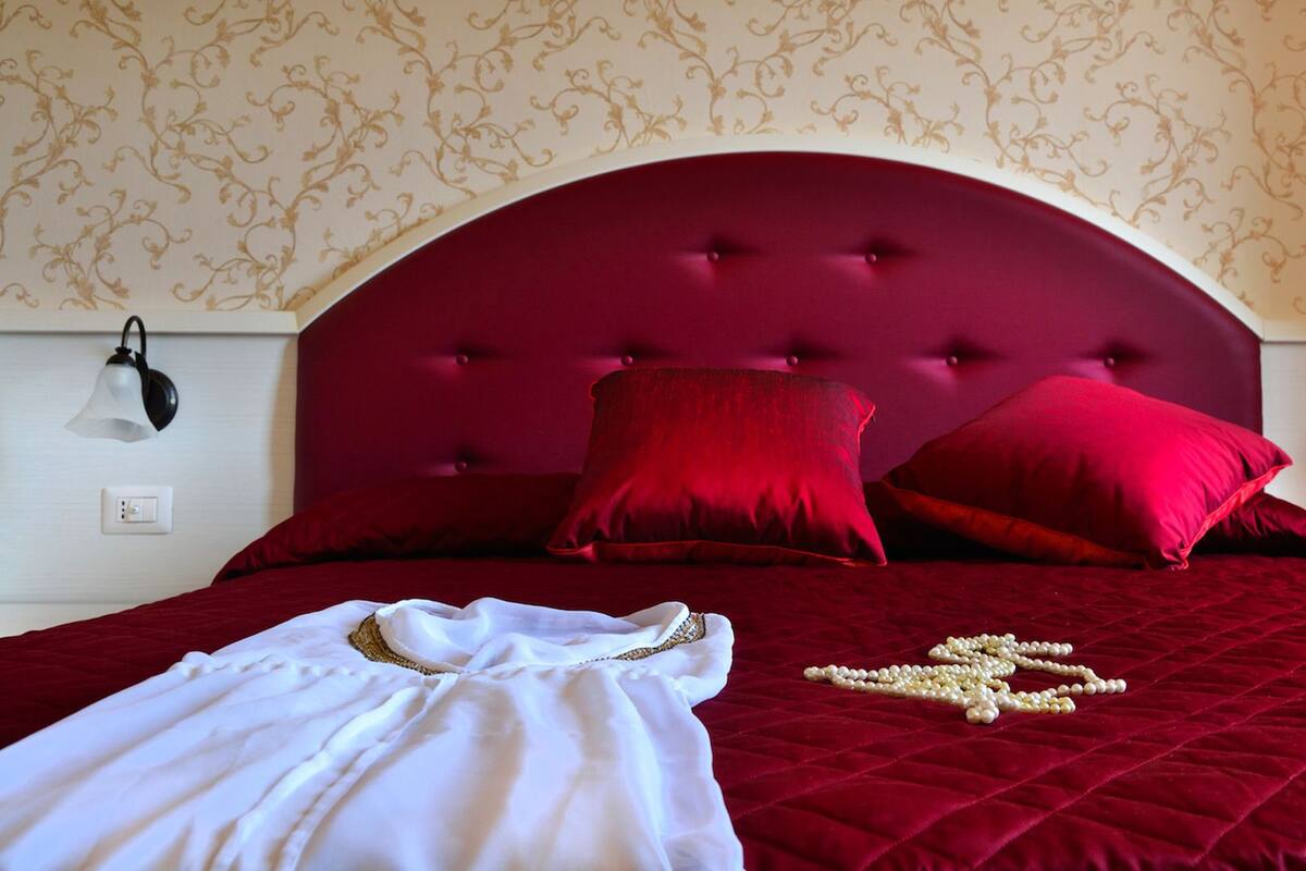 A bed with a red headboard, red pillows, and a white garment on the bed.