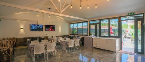 A modern hotel lobby with a seating area, a TV screen, and large windows.