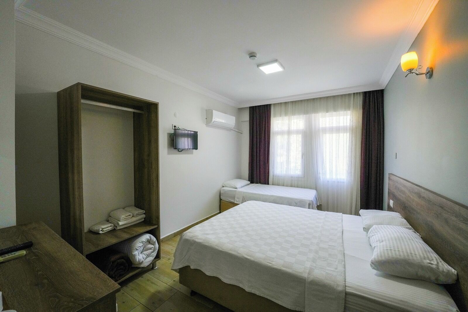 Una camera d'albergo con due letti, un armadio, una TV e una finestra con tende.