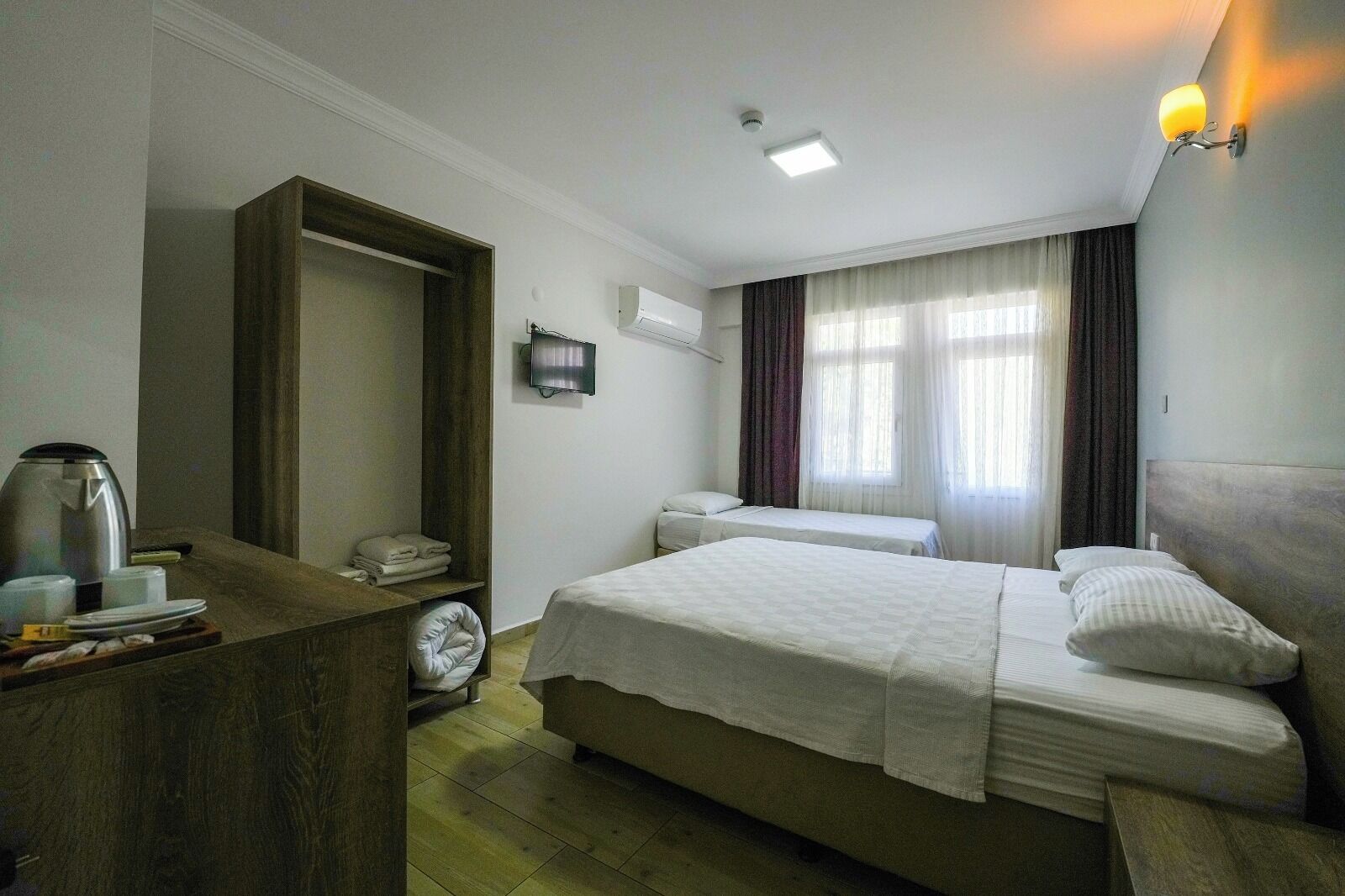 Habitación de hotel con cama, mesitas de noche, escritorio con tetera, televisión y ventana con cortinas.