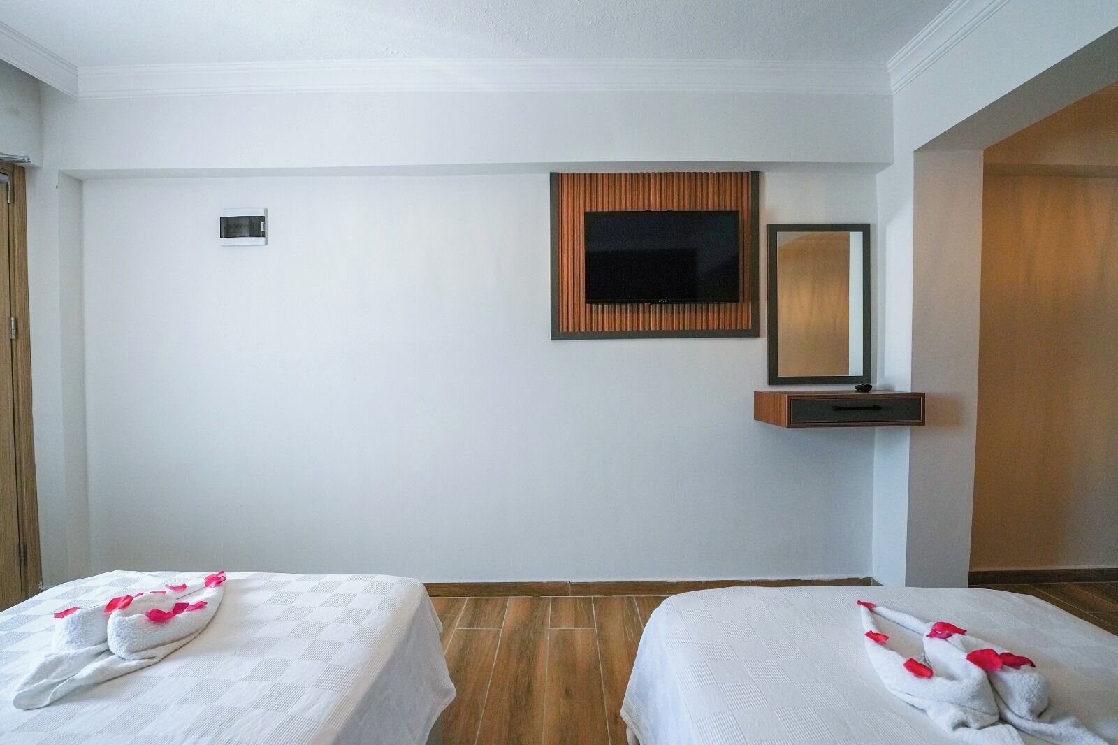 A hotel room with two beds, a TV, a mirror, and a small shelf.