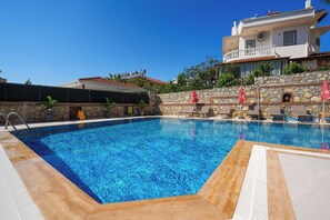 A swimming pool with lounge chairs and umbrellas, a stone wall, and a building with a balcony. - Mut Hotel (Fethiye)