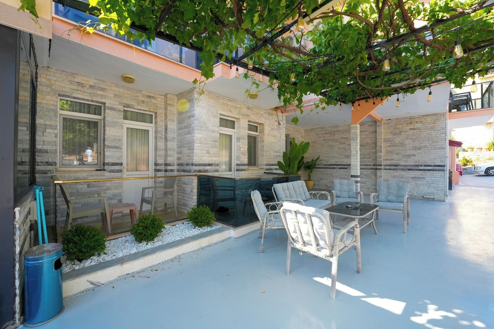 A covered outdoor seating area with a table and chairs, a potted plant, and a stone wall.