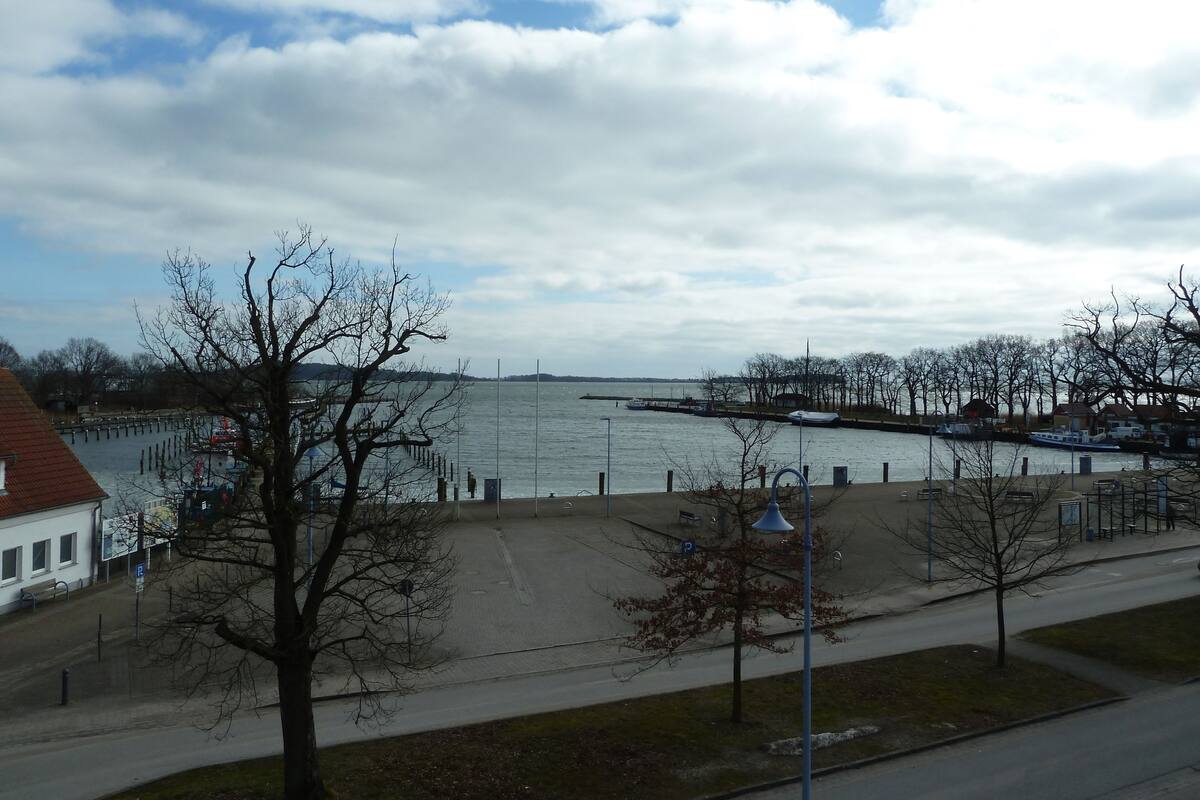 A waterfront view with a dock, a pedestrian path, and a row of buildings.