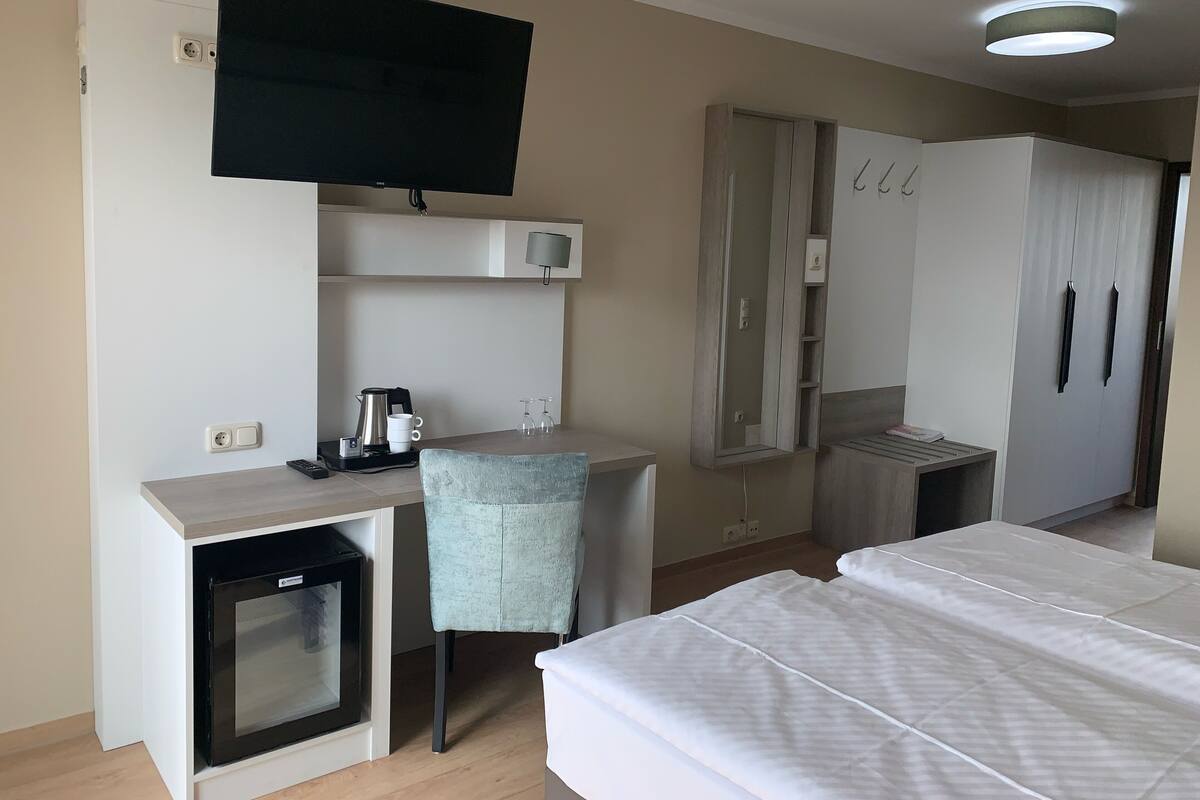 A hotel room with a bed, a desk with a chair, a television, a minibar, and a wardrobe.