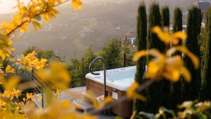 A hot tub on a deck with a view of a valley and distant buildings. - Apartments Prairerhof (Schenna)
