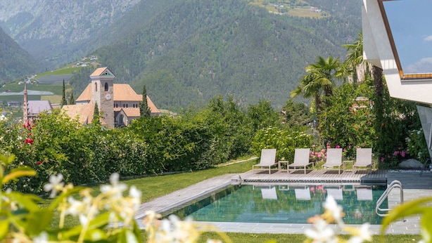 A swimming pool with lounge chairs, surrounded by lush greenery and a mountain backdrop. - Apartments Prairerhof (Schenna)
