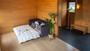 A modern bedroom with a bed, a seating area, a potted plant, and a mirror. - Apartments Prairerhof (Schenna)