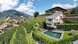 A modern hotel with a swimming pool, surrounded by lush greenery and mountains. - Apartments Prairerhof (Schenna)