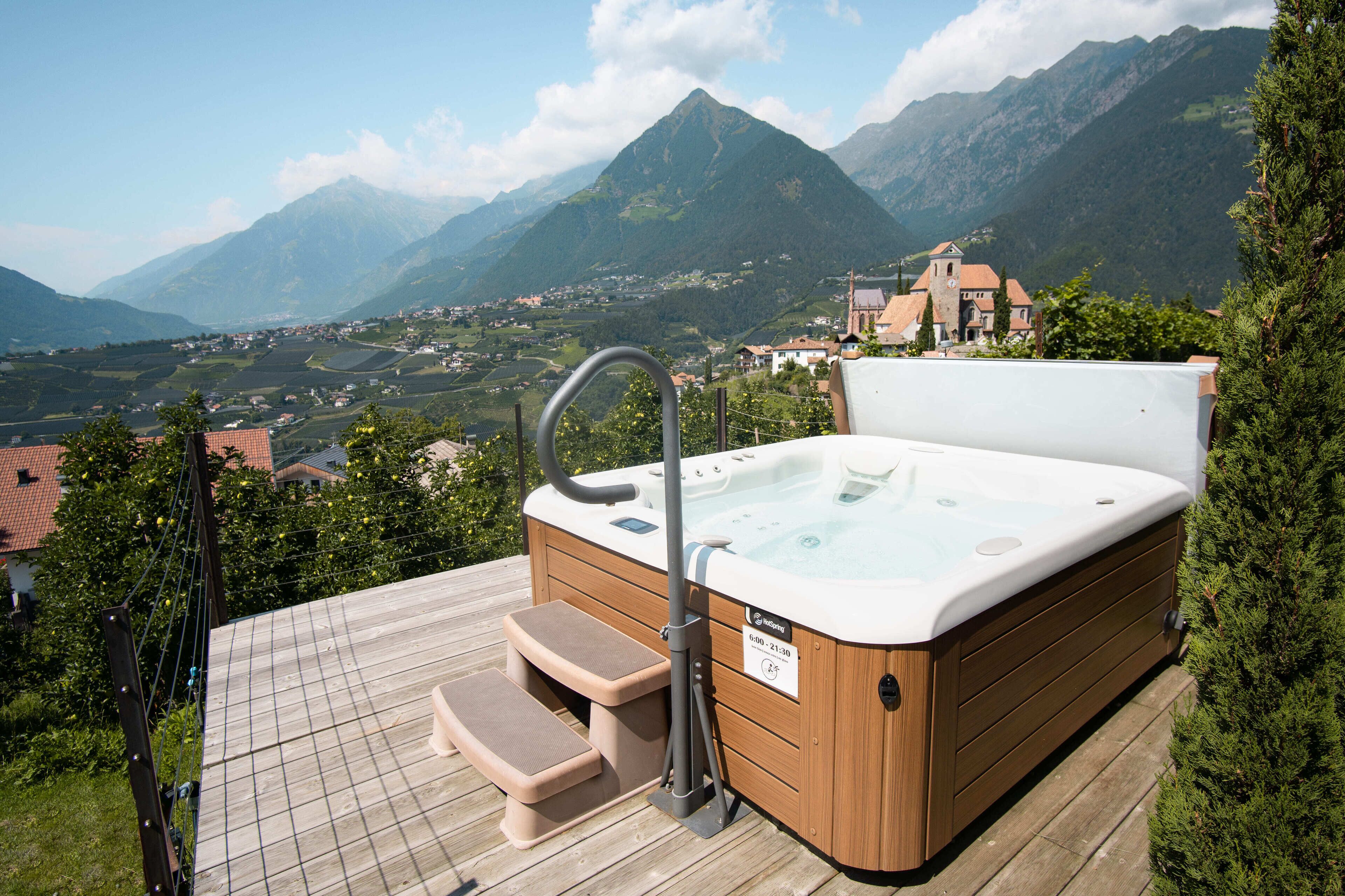 A hot tub on a wooden deck with a view of mountains and a village.