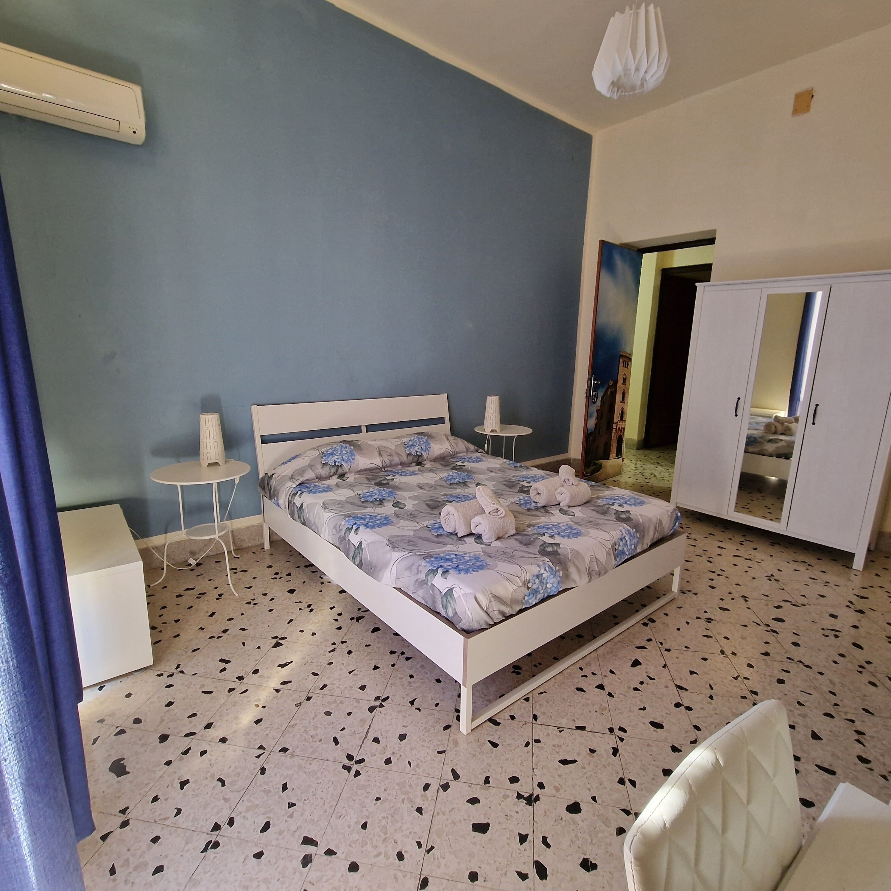 Una camera da letto con un letto, un tavolino, una sedia, un armadio e una ventola a soffitto.