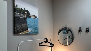 A bathroom with a painting of a coastal scene, a round mirror, and a white vanity with a light.