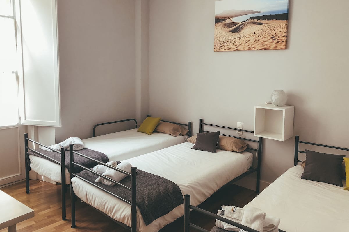 Une chambre avec deux lits simples, une étagère blanche avec une lampe et un tableau représentant une scène de plage.
