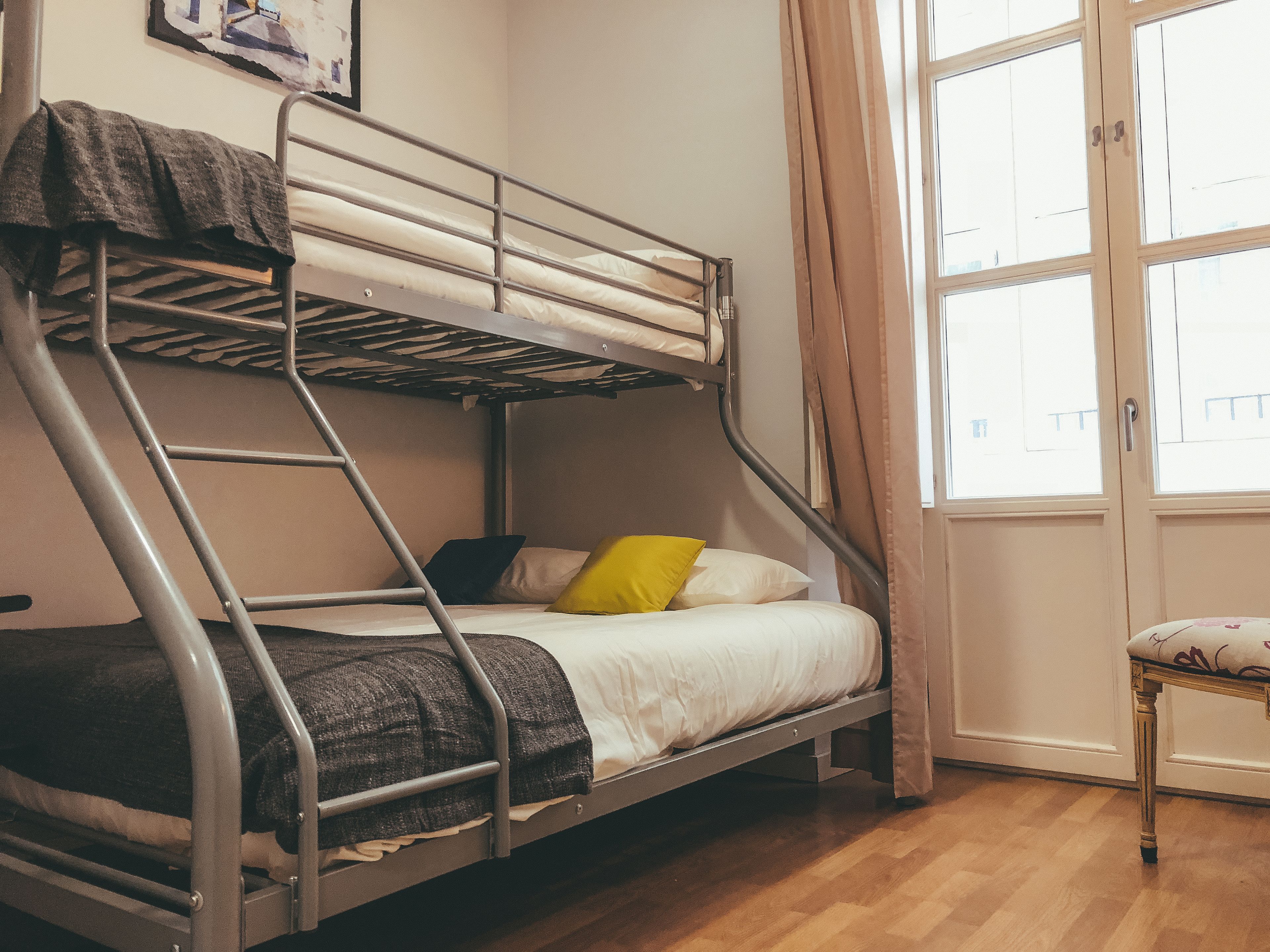Een stapelbed met een ladder, een klein tafeltje en een raam met gordijnen.