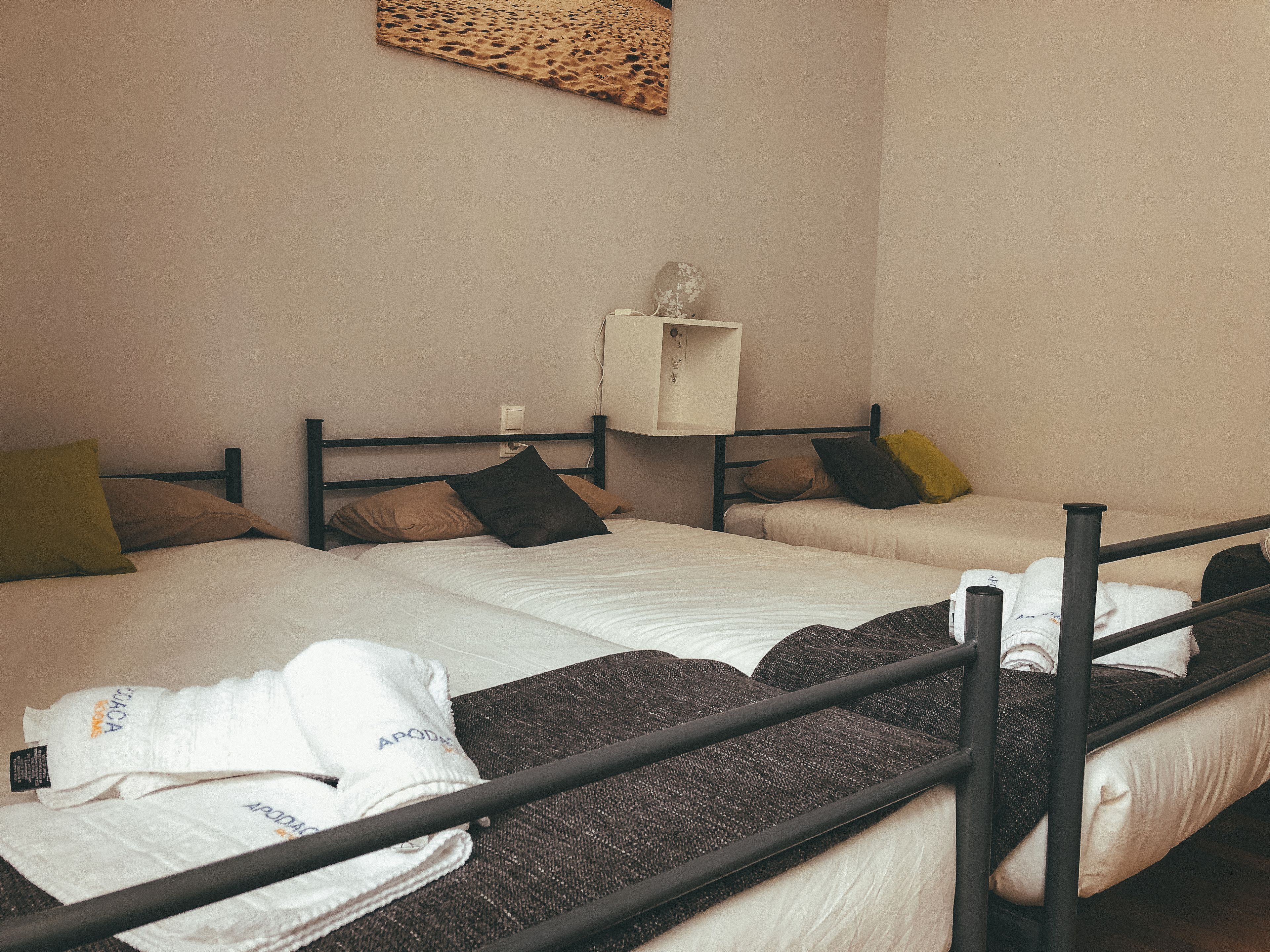 Ein Hotelzimmer mit zwei Betten, einem kleinen weißen Schrank und einem an der Wand befestigten Regal.