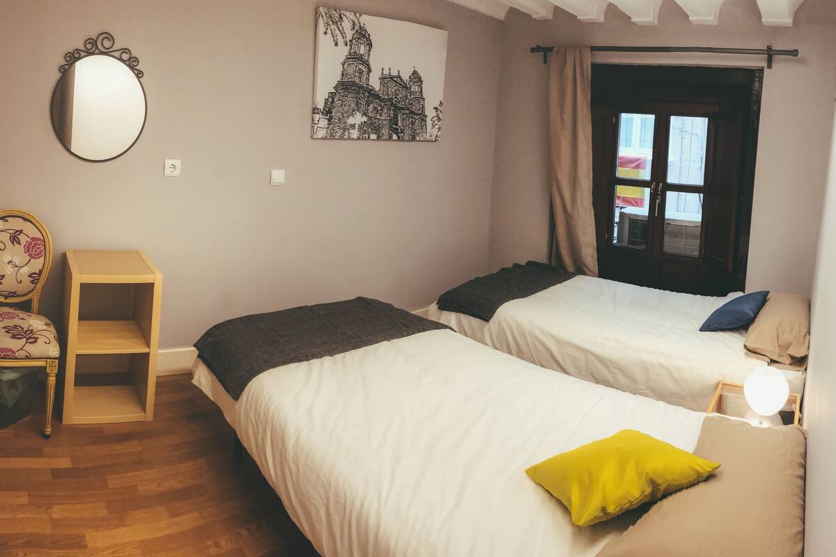 Une chambre avec deux lits, une chaise, un miroir et un mur orné d’un tableau.