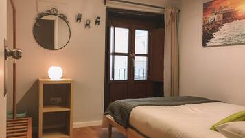 Un dormitorio con cama, mesita de noche con lámpara, espejo y ventana con cortinas.