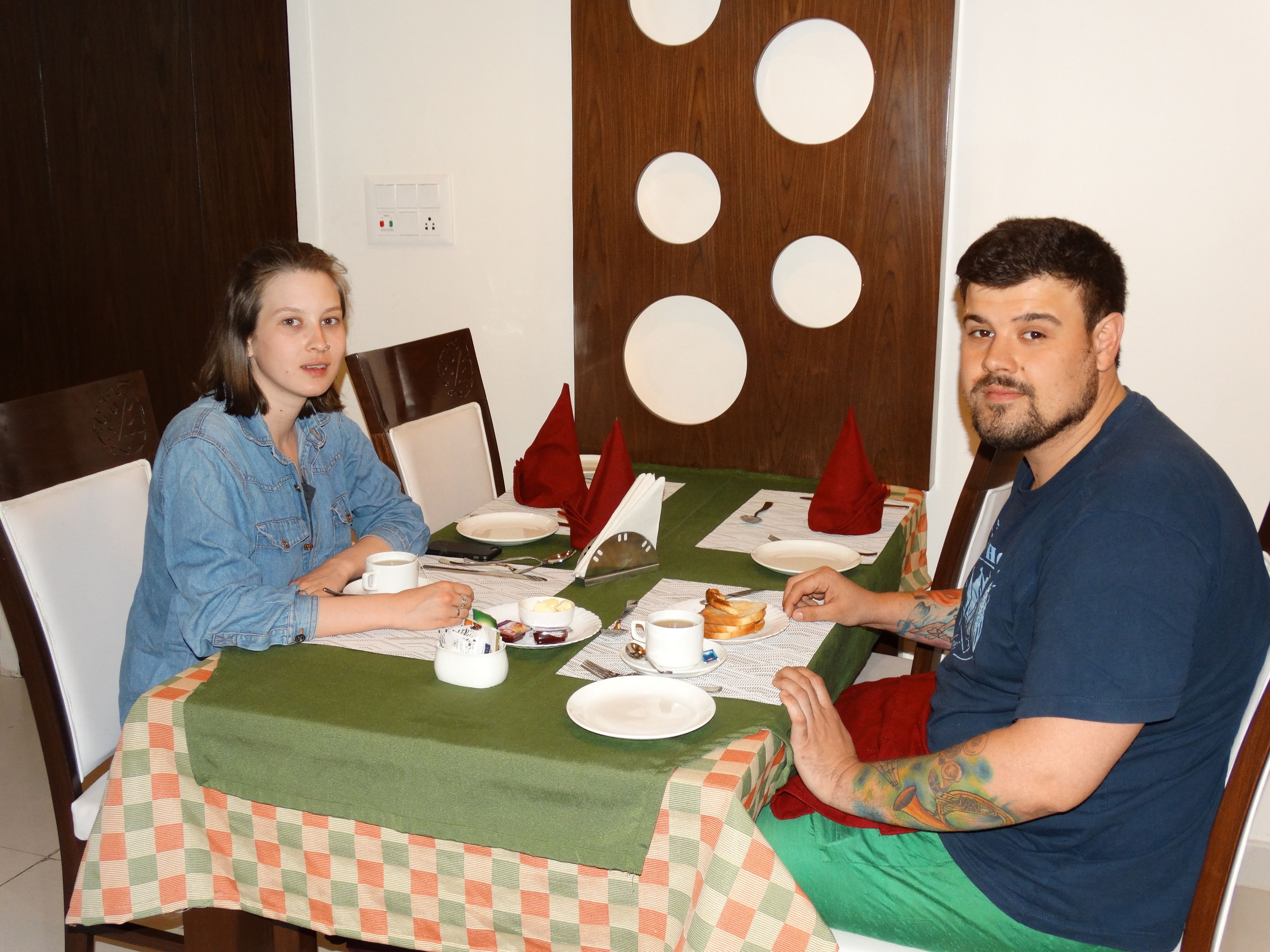 A dining table with a green tablecloth, white plates, and red napkins.
