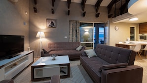 A modern living room with a flat-screen TV, sofas, a coffee table, and a dining area with a kitchen in the background.