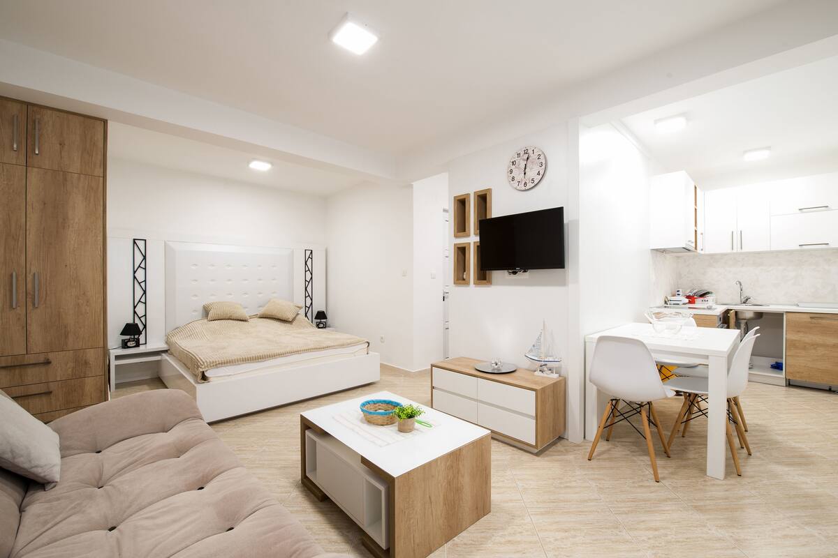 A modern, well-lit bedroom with a bed, bedside table, and a small desk with a chair.