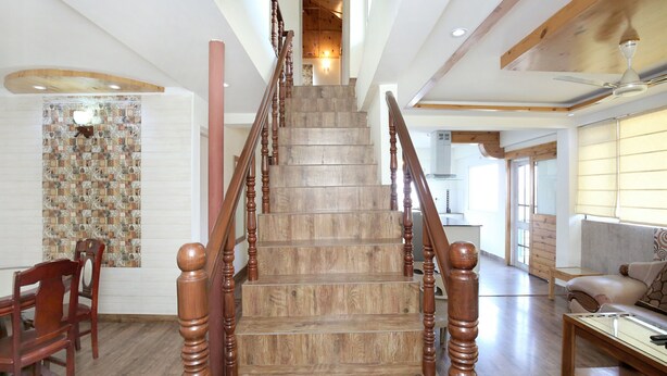 A wooden staircase with a handrail, leading to a landing with a view of a kitchen and living area. - OYO 12185 Home Wayside Villa 3BHK Apartment Kasauli (Kasauli)