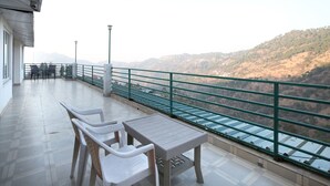 A balcony with a table and chairs, overlooking a hilly landscape. - OYO 12185 Home Wayside Villa 3BHK Apartment Kasauli (Kasauli)
