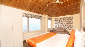 A bedroom with a wooden ceiling, a bed with an orange bedspread, a window with a floral valance, and a sofa with a floral-patterned curtain. - OYO 12185 Home Wayside Villa 3BHK Apartment Kasauli (Kasauli)