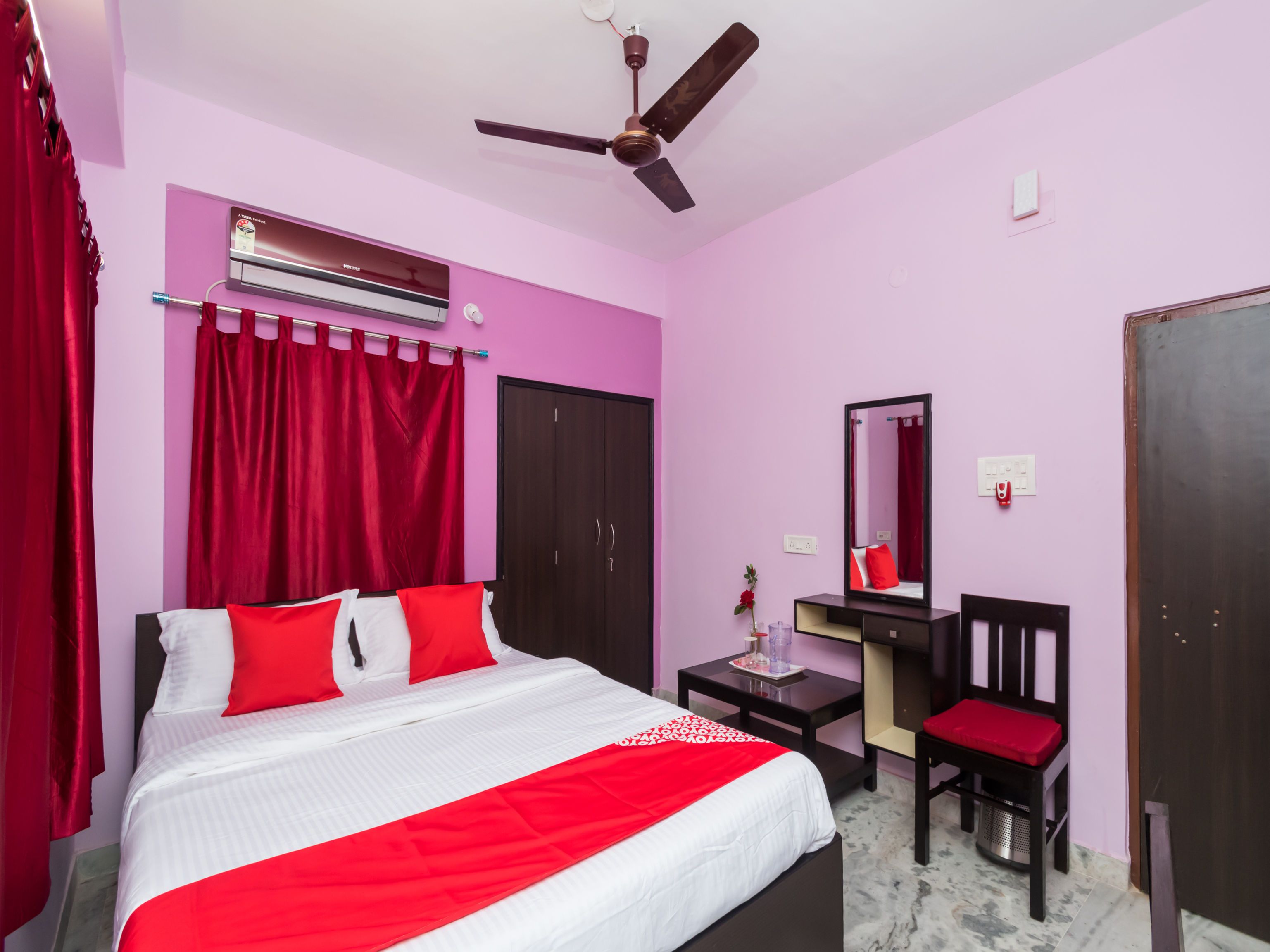 A bedroom with a bed, a desk, a chair, a mirror, a wardrobe, and a ceiling fan.