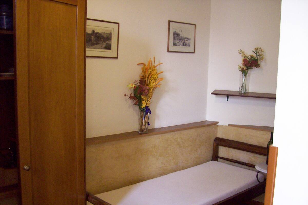 Une pièce comprenant un banc en bois, une petite table et un vase avec des fleurs posé sur une étagère.