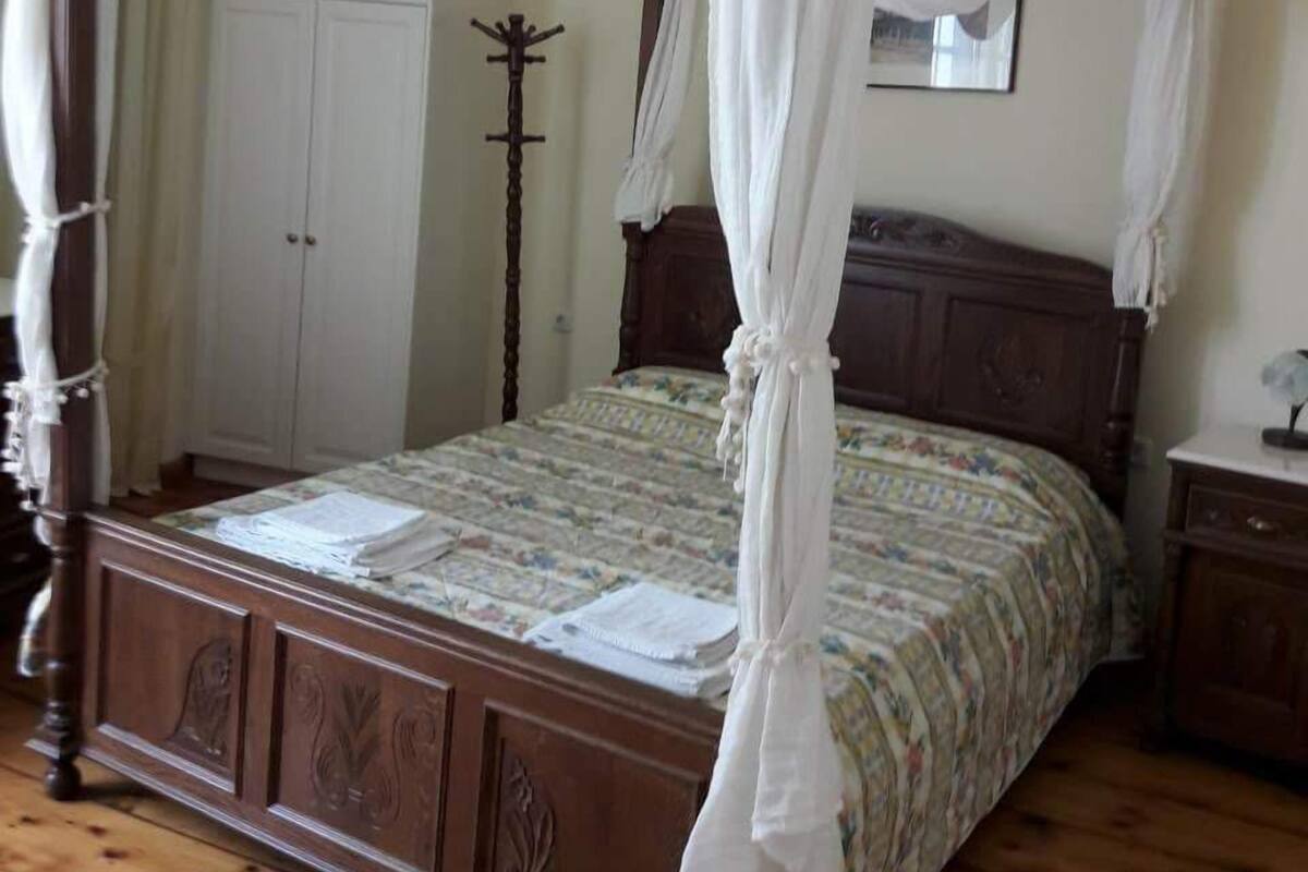 Un lit à baldaquin à quatre poteaux, agrémenté d’une couvre-lit à motifs floraux, d’une tête de lit en bois et d’une table de chevet avec une lampe.