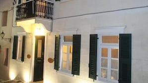 A two-story building with white walls and green shutters, featuring a balcony with a black railing.