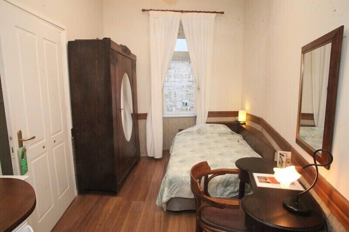 Une petite chambre à coucher, chaleureuse et accueillante, avec un lit, une armoire en bois, un bureau avec une chaise et un miroir.