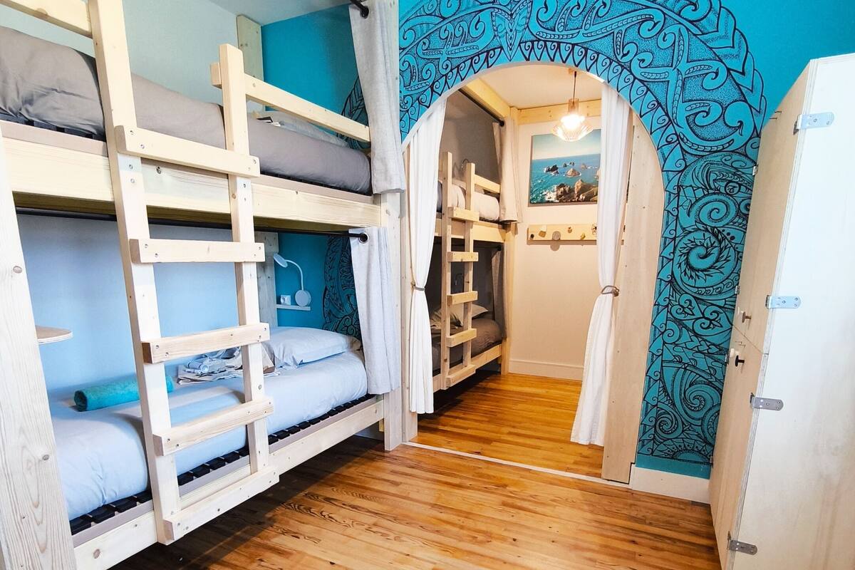Una habitación con literas, suelo de madera y pared azul con un arco decorativo.